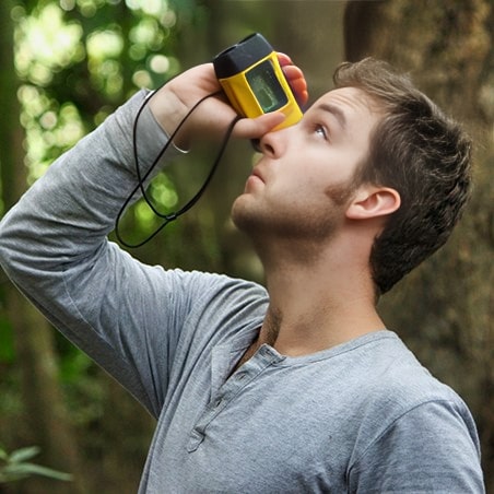 A young man looking up at a tree through a pocket telescope.