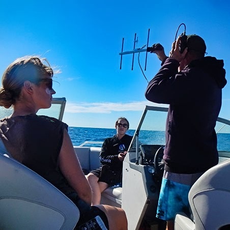 Three people on a boat; one with a radio transmitter for research purposes.