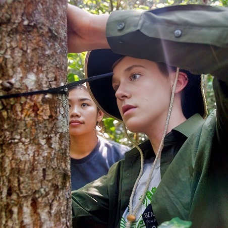 Two young adults measuring a tree trunk's width.