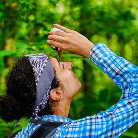 A woman looking up at the tops of trees with a pocket telescope.