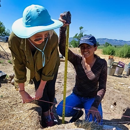 Two girls measuring the depth an archaeological dig site in Colorado.