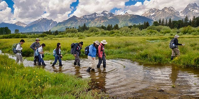 A group of teens wading through the water during a hike in the Rockie Mountains