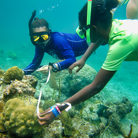 Two teen girls measuring a colorful coral reef underwater (C) Amanda Lowder | Earthwatch.